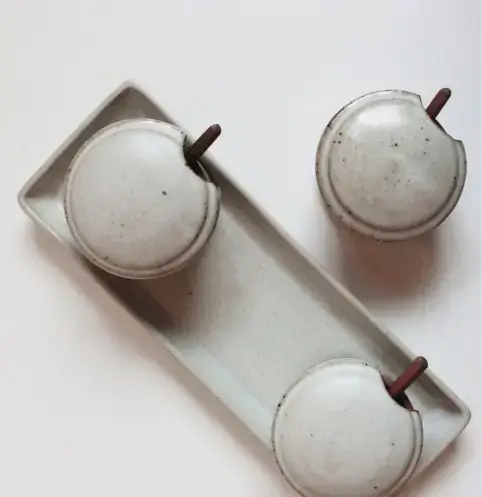 A speckled white ceramic mug with a terracotta colored base sits on a matching speckled white saucer against a plain white background.