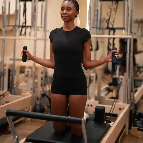 Woman doing Pilates on reformer with 1kg hand weights from Revival Studio